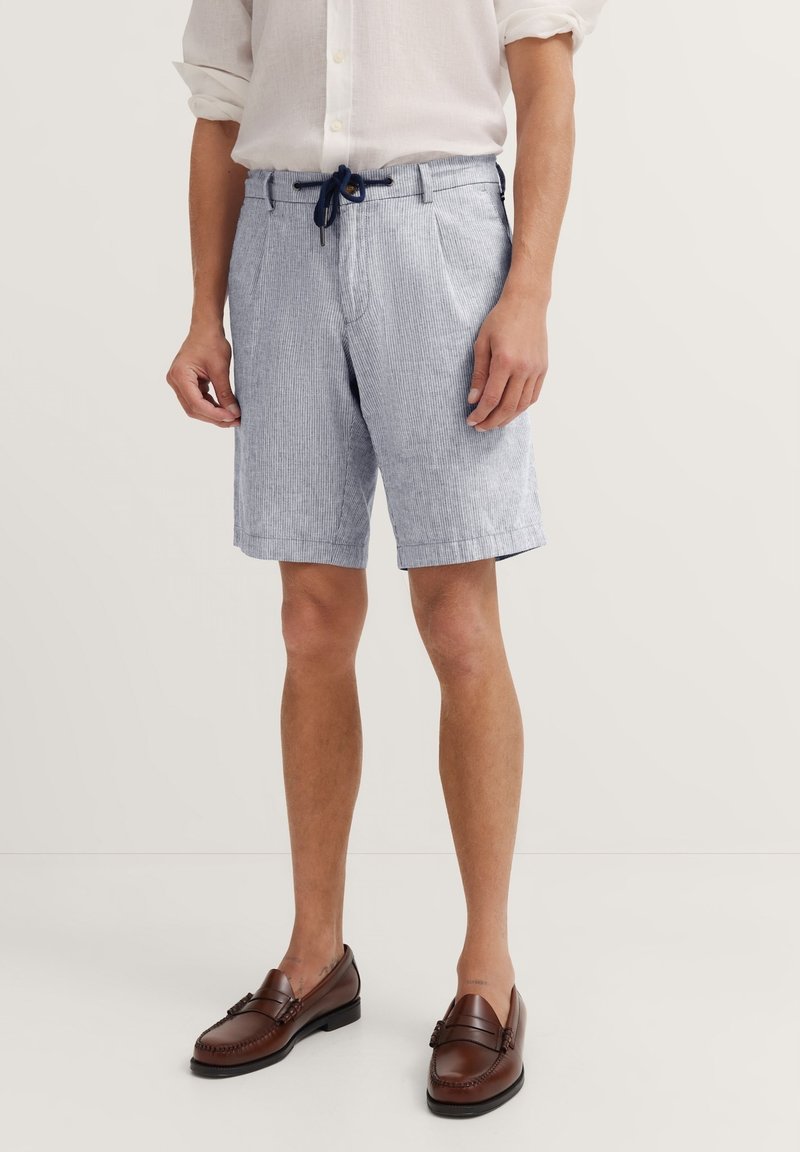 Helle blaue gestreifte Shorts mit einem Kordelzugbund, seitlichen Taschen und einem lockeren Schnitt, kombiniert mit braunen Lederloafers.