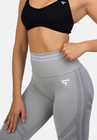 Szare legginsy o wysokim stanie z prążkowaną fakturą, akcentem z logo i kontrastowymi paskami. W połączeniu z czarnym biustonoszem sportowym.