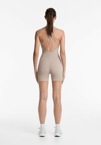 Beige rompi ketat dengan punggung rendah dan desain tali silang, menampilkan panjang pendek dan tekstur halus.