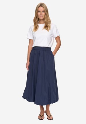 Jupe mi-mollet bleu marine en tissu léger, taille élastique, poches, associée à un t-shirt blanc et des tongs noires.