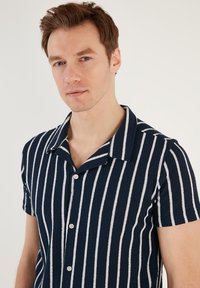 Camicia a maniche corte a righe blu navy e bianche con colletto, realizzata in tessuto testurizzato, con chiusura a bottoni e vestibilità rilassata.