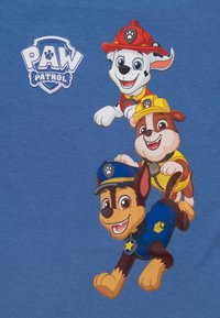 Camicia di cotone blu con tre cani dei cartoni animati di PAW Patrol. I personaggi sono illustrati con colori vivaci e espressioni giocose.