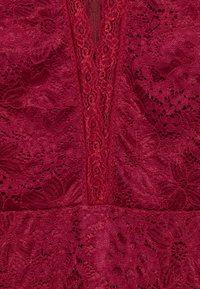 Bordeaux kantstof met bloemmotieven heeft een centraal paneel van gestructureerd kant, dat ingewikkelde details en gelaagd ontwerp benadrukt.