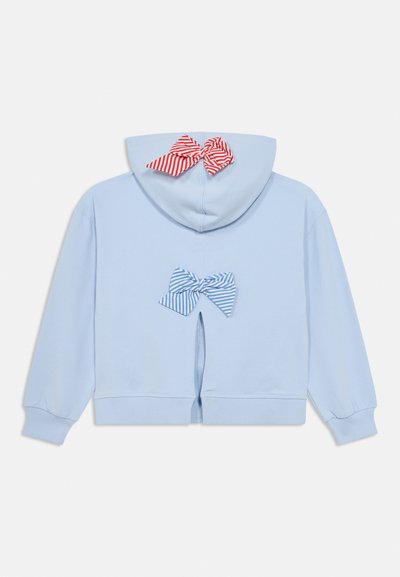 Ανοιχτό μπλε φούτερ με ριγέ μπλε και λευκή φιόγκο στο πίσω μέρος, με έναν κόκκινο και λευκό ριγέ φιόγκο στη κουκούλα. Μαλακό ύφασμα, χαλαρή εφαρμογή.