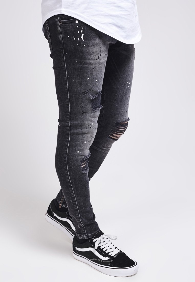 Zwarte gescheurde jeans met verfspatten, slim fit, met verschillende versleten plekken. Gecombineerd met zwart-witte sneakers.