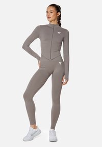 Gray athletic full-zip top and high-waisted leggings. Smooth, stretchy fabric with a fitted design. White logo accents on chest and waist.