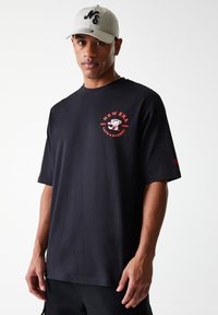 Black cotton t-shirt with short sleeves and a round neckline, featuring a red graphic logo and text on the front. Accompanied by a light cap.