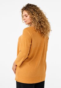 Sennepsfarvet stribet sweater med teksturerede vertikale og horisontale ribmønstre, der har trekvartærmer og en afslappet pasform.