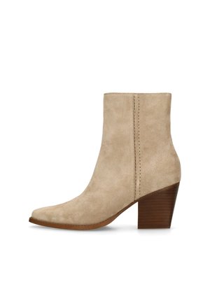 Bottine en daim beige avec bout pointu et talon bloc en bois superposé, présentant une couture verticale sur le côté.