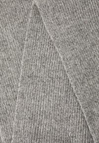 Tissu tricoté gris avec une texture en relief, offrant une apparence douce et chaleureuse. Les fibres sont entrelacées avec des fils plus sombres pour plus de profondeur.