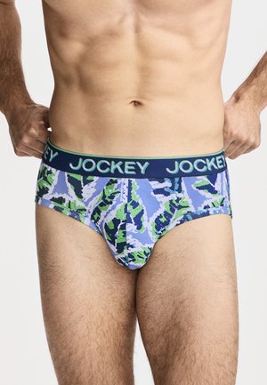 Männlicher Oberkörper mit blau-grün gemusterten Slips mit Navy-Bund und "Jockey"-Logo, Hände passen den Bund an beiden Seiten an.