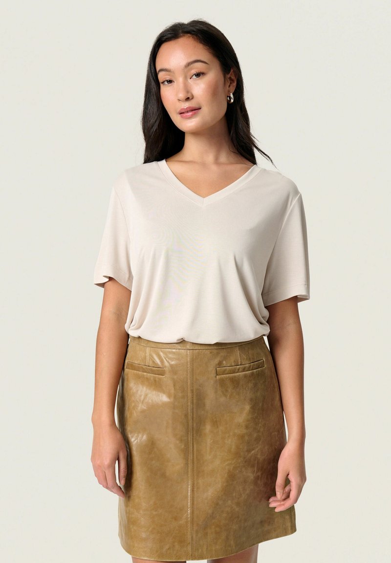 T-shirt beige a scollo a V con maniche corte abbinato a una gonna in pelle marrone a vita alta con due tasche frontali e una texture liscia.