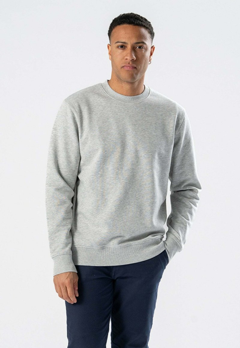 Lysegrå crewneck sweatshirt lavet af bomuldsblandingsmateriale med ribbede manchetter og kant. Modellen står i marineblå bukser med hænderne i lommerne.