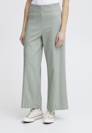 Groene geruite wijde broek gemaakt van lichtgewicht stof; heeft een hoge taille en wordt gecombineerd met witte sneakers.