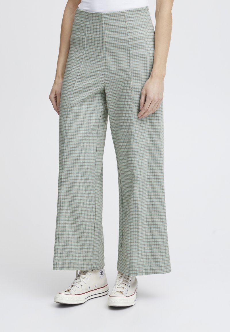 Pantalons large à carreaux verts en tissu léger ; taille haute et associés à des baskets blanches.