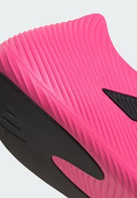 Leuchtend pinker Sneaker mit strukturierter Oberfläche, Wellenmustern, schwarzer Sohle und einem schwarzen Logo-Akzent an der Seite.