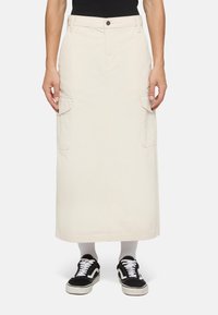 Beige cargo kjol med rak silhuett, med sidofickor och knappstängning, ihop med svarta sneakers och vita strumpor.