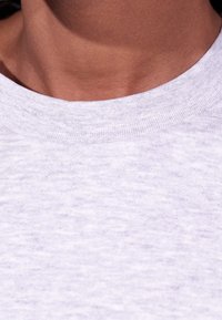 Primer plano del cuello y la parte superior del pecho de una persona que lleva puesta una camiseta de cuello redondo en color gris claro.