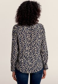 Cremfarbene Button-Down-Bluse mit marineblauem Blattmuster. Lange Ärmel, weicher Stoff, abgerundeter Saum und Detail mit einer Rückentasche.