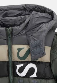 Giacca imbottita con un mix di pannelli verde scuro, neri e beige. Include una cerniera frontale, dettagli in velcro e un design con colletto alto.