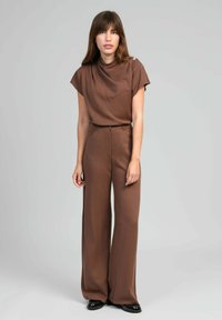 Ensemble marron en deux pièces comprenant un haut à manches courtes avec un col drapé et un pantalon à jambes larges. Le tissu semble lisse avec un léger brillant.
