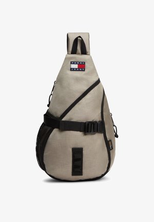 Beige Tommy Jeans Umhängetasche mit schwarzem Besatz, verstellbarem Gurt, Schnalle, Netzseitentasche und vorderem Logo-Patch.