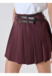 Gonna plissettata bordeaux con due cinture—una marrone e una grigia—con dettagli in metallo dorato. Tessuto liscio con pieghe nette e vita aderente.