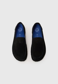 Sorte slip-on sko laget av semsket skinn, med en glatt overflate, rund tå og kontrastfarget blå innersåle. Stikningene omrammer de øvre kantene.
