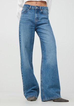 Jeans svasati a vita alta di colore blu chiaro con un classico design a cinque tasche e texture sbiadita. Include passanti per la cintura e chiusura con bottone in metallo.