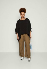 T-top preto oversized com mangas largas, combinado com calças largas em caqui. Os acessórios incluem uma pequena bolsa azul e tênis cinzentos.