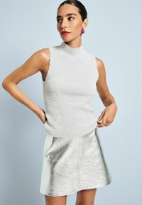 Grijze mouwloze top met een gestructureerde afwerking, gecombineerd met een glanzende metallic zilveren minirok. Decoratieve roze oorbellen en gouden ringen.