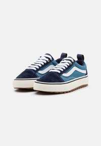 Blå ruskinn sneakers med hvite detaljer, med en tykk hvit såle, runde snøresko og en løpepropp på hælen for enkel påkledning.