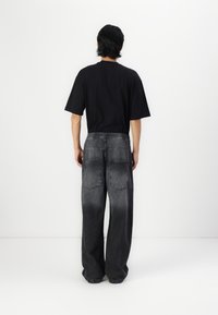Black short-sleeve t-shirt paired with loose, faded black denim pants featuring an elastic waistband and two back pockets.