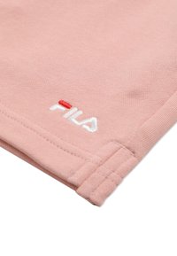 Gros plan sur un tissu rose avec le logo FILA blanc et rouge cousu près de l'ourlet et un détail de couture double.