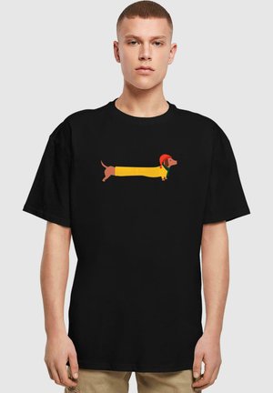 Black t-shirt featuring a playful graphic of a dachshund in a yellow costume with a red hat. Short sleeves, standard fit, cotton material.