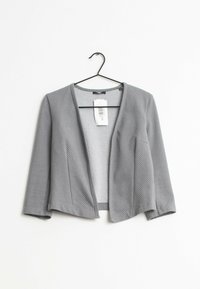 Grå, prickig kort jacka med lös passform, öppen fram och trekvartslånga ärmar, hängande på en svart krok mot en vit bakgrund.