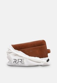 Braune Lederbrieftasche mit eingeprägtem PURE-Logo, teilweise in einem weißen Zugbeutel mit der Aufschrift PURE Leather Studio.