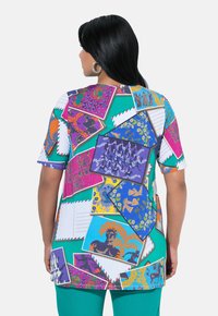 Top de jersey multicolor con un collage de postales estampadas, tonos vibrantes como verde, rosa y azul, con mangas cortas y un corte relajado.