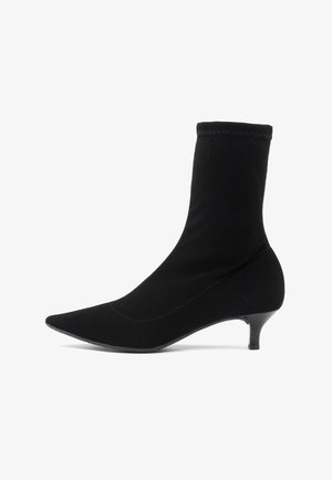 Juodas kulkšninis botas, pagamintas iš minkštos medžiagos, su smailiu pirštu ir plonu kulnu. Yra prigludusi kojelė ir be siūlių dizainas, suteikiantis elegantišką išvaizdą.