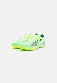 Zapatillas deportivas de color verde neón con parte superior de malla texturizada, detalle de raya negra y acentos en azul contrastante. Suela de goma con relieve para mayor agarre.