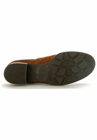 Chaussure en daim marron avec une semelle en caoutchouc à motifs présentant diverses textures d'adhérence. Le talon est bas et l'intérieur affiche le marquage de la marque.