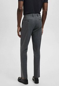 Pantaloni gri, croiți pe măsură, cu o tăietură slim, având un față plată, două buzunare la spate cu închidere prin buton și o textură netedă.