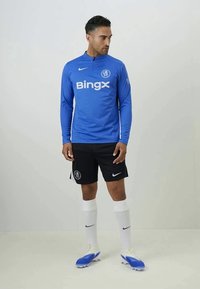 Modrá športová dlhá košeľa s logom "Bingx", čierne šortky, biele ponožky a modré kopačky. Obsahuje logo Nike na oblečení a šortkách.