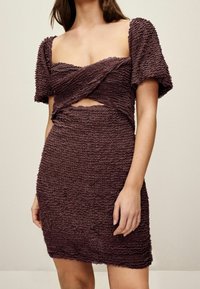 Robe violette texturée avec des manches courtes bouffantes, un design avant torsadé et un détail découpé à la taille, présentant une silhouette ajustée.