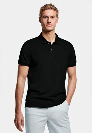 Schwarzes Poloshirt aus strukturiertem Stoff, mit einem Knopfkragen, kurzen Ärmeln und einem geraden Saum, kombiniert mit hellen Shorts.