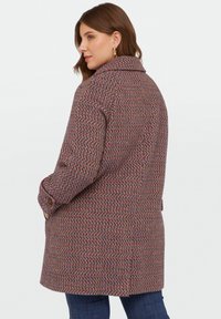 Palton țesut cu un model houndstooth în violet, portocaliu și albastru. Dispune de o guler clasic și manșete cu nasturi, având o croială dreaptă și lejeră.