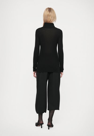 Crna turtleneck majica, dugi rukavi, uski kroj. Uparena sa širokim crnim hlačama i crnim štiklama. Gladak materijal, minimalni dizajn.