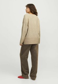 Beige stickad tröja med lös passform, ribbad nederkant och sänkta axlar. Kombination med bruna vida byxor och röda platta skor.