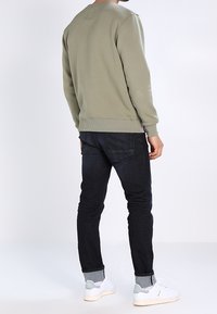 Pull verde oliva con polsini e orlo a coste; abbinato a jeans in denim scuro e sneaker bianche con accenti grigio chiaro.