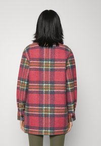 Red plaid wool coat with green, yellow, and blue accents. Features long sleeves, buttoned cuffs, and a straight cut. View from the back.